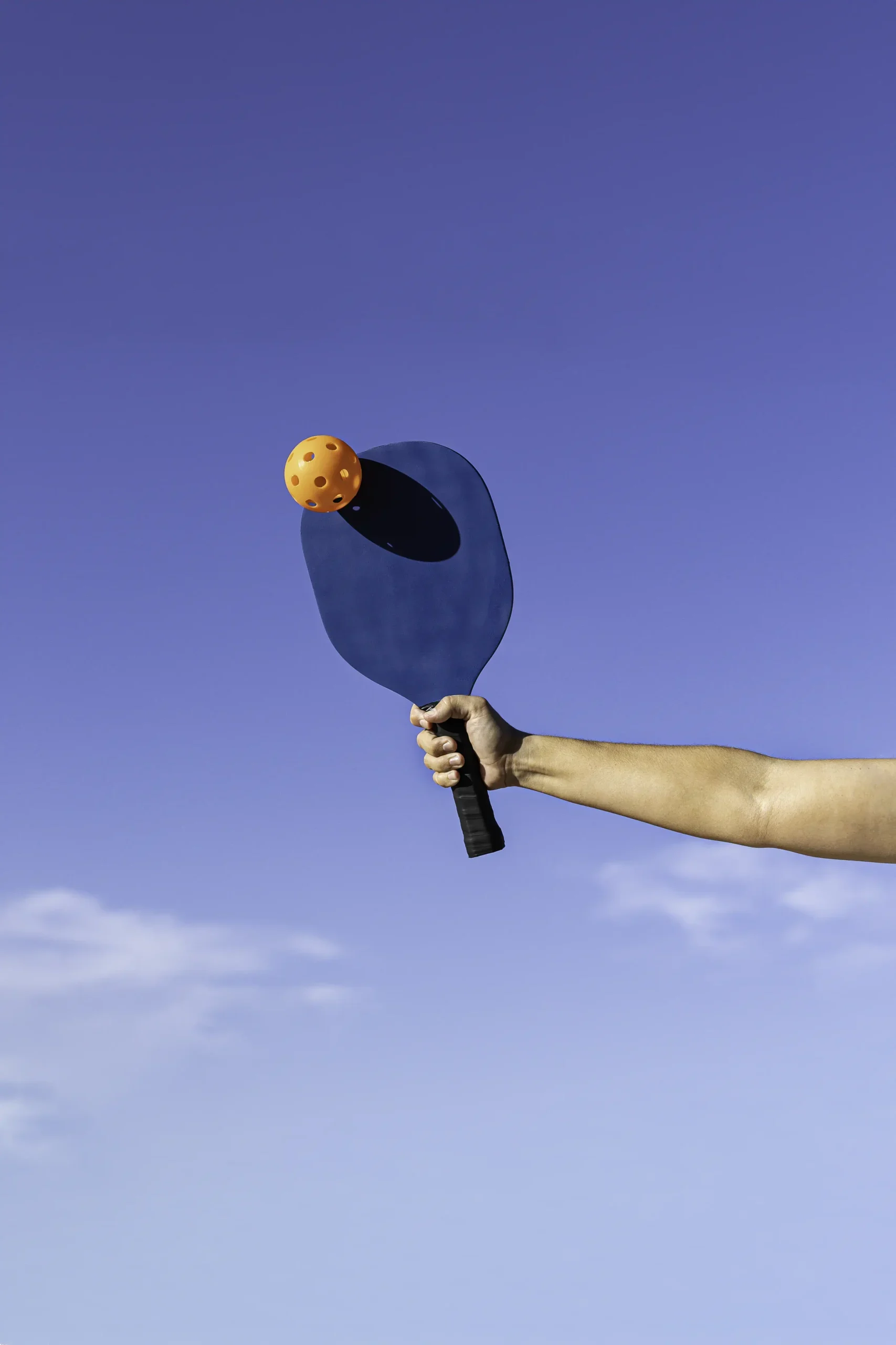 arm-with-blue-paddle-hitting-orange-pickleball-ball